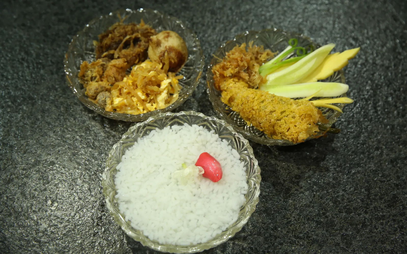 ข้าวแช่น้ำดอกไม้ในถ้วยแก้วใสพร้อมเครื่องเคียงหลากสีสันเรียงบนจาน