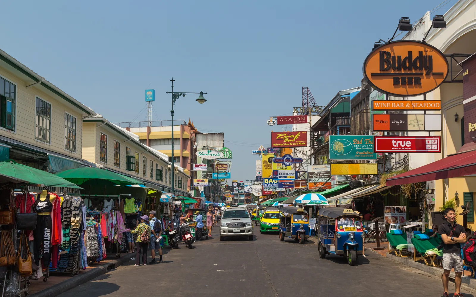 ถนนข้าวสารกรุงเทพฯ ยามค่ำคืน ป้ายไฟสีสันและร้านค้าเรียงรายสองฝั่ง คึกคักเต็มไปด้วยนักเที่ยว
