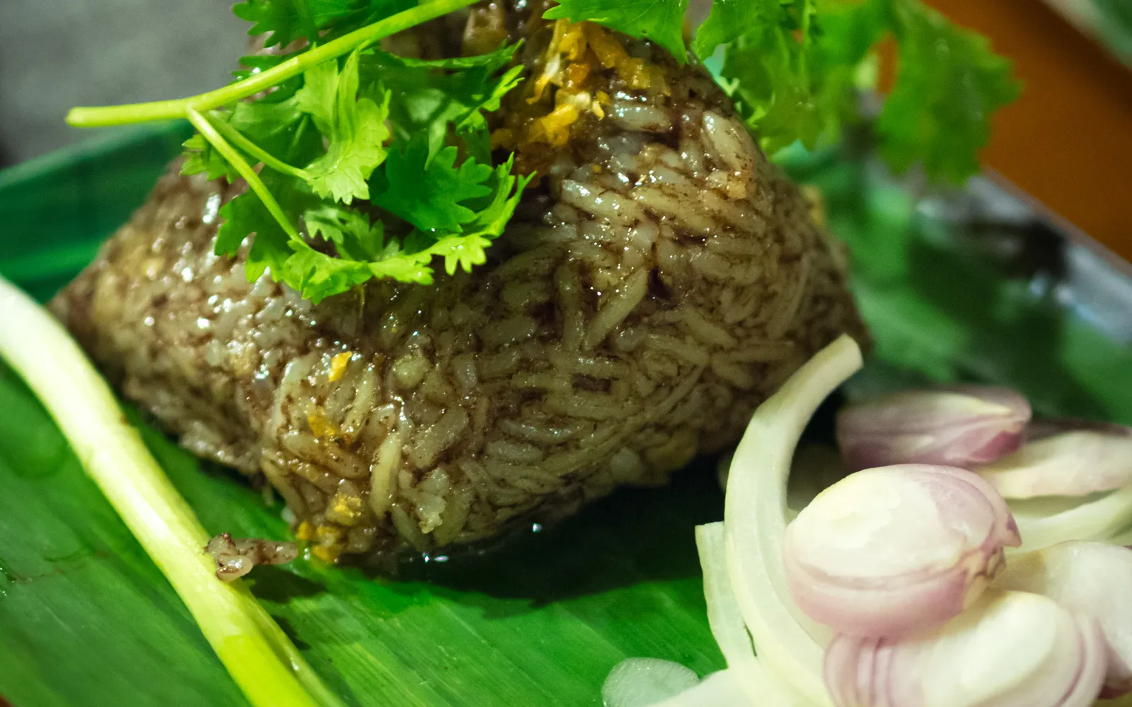 ข้าวกั๊นจิ๊นห่อใบตอง ห่อข้าวเหนียวสีแดงเข้มผสมเลือดหมูและหมูสับ เสิร์ฟบนใบตองสด