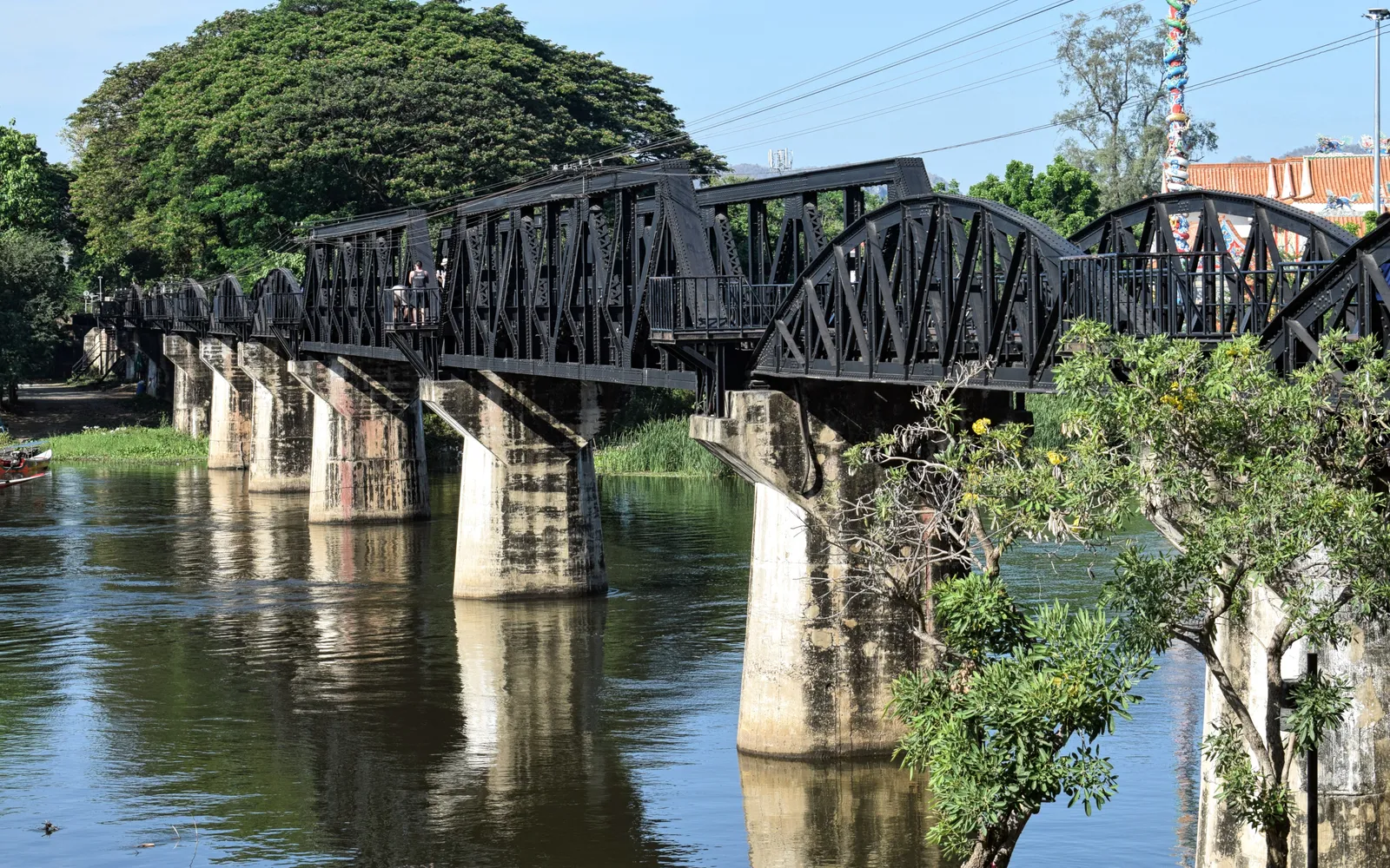 สะพานรถไฟถ้ำกระแซโค้งเลาะหน้าผาริมแม่น้ำแควน้อย ฉากหลังเป็นป่าเขียว