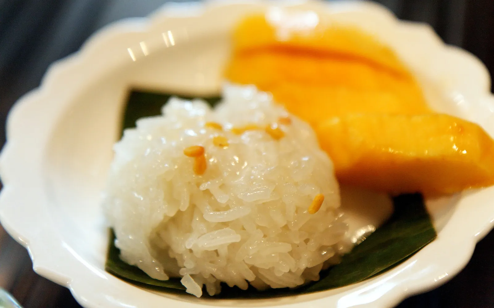 ข้าวเหนียวมะม่วงน้ำดอกไม้สุกสีเหลืองสด ข้าวเหนียวมูนขาวนวลราดกะทิข้น เสิร์ฟในจานกล้วยไม้