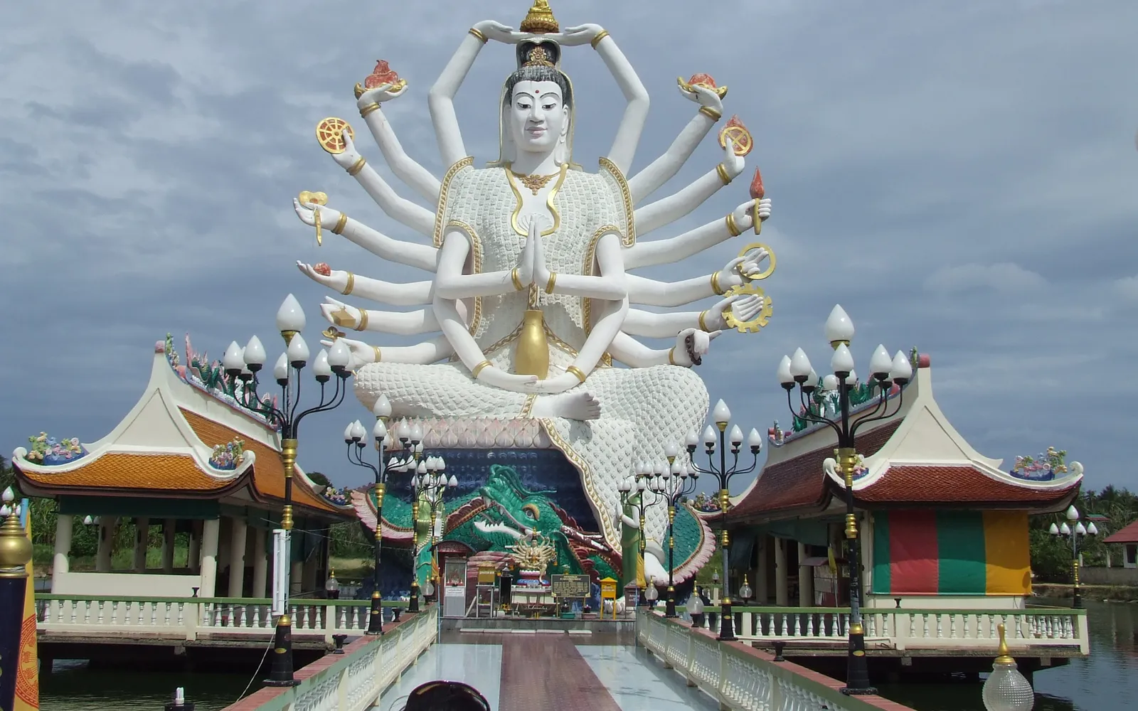 วัดปลายแหลมเกาะสมุย รูปปั้นเจ้าแม่กวนอิม 18 แขนสีขาวขนาดใหญ่ตั้งอยู่กลางสระน้ำ ท้องฟ้าสีฟ้า