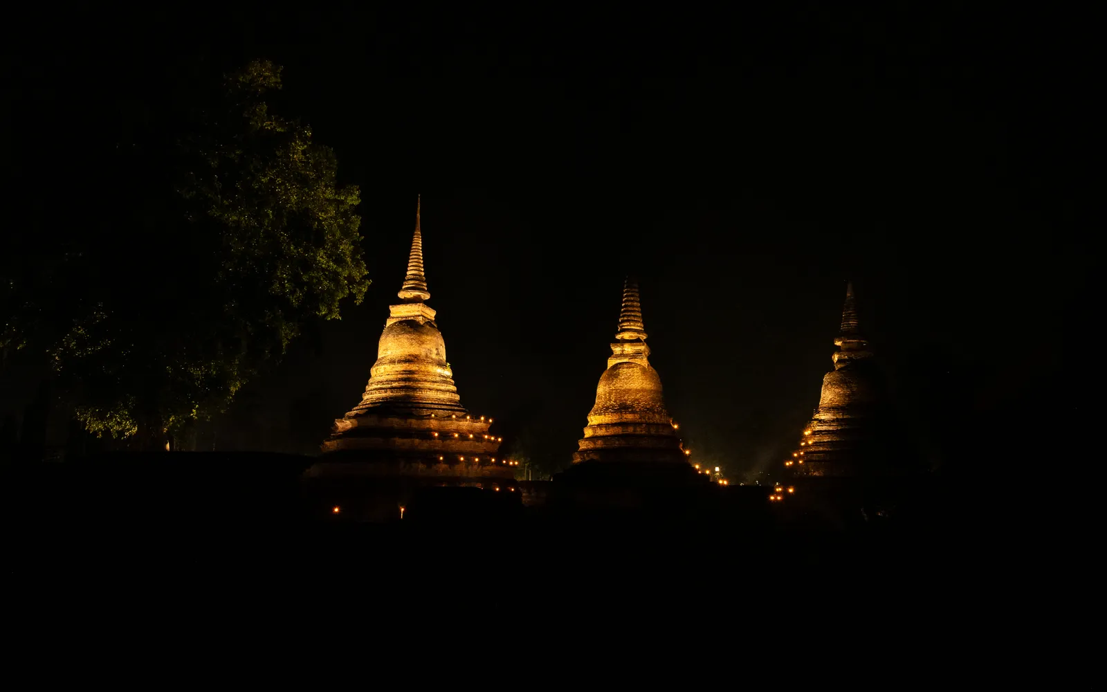 กระทงและโคมไฟลอยอยู่บนสระตระพังท่ามกลางโบราณสถานสุโขทัยที่ส่องไฟสว่างไสวยามค่ำคืน