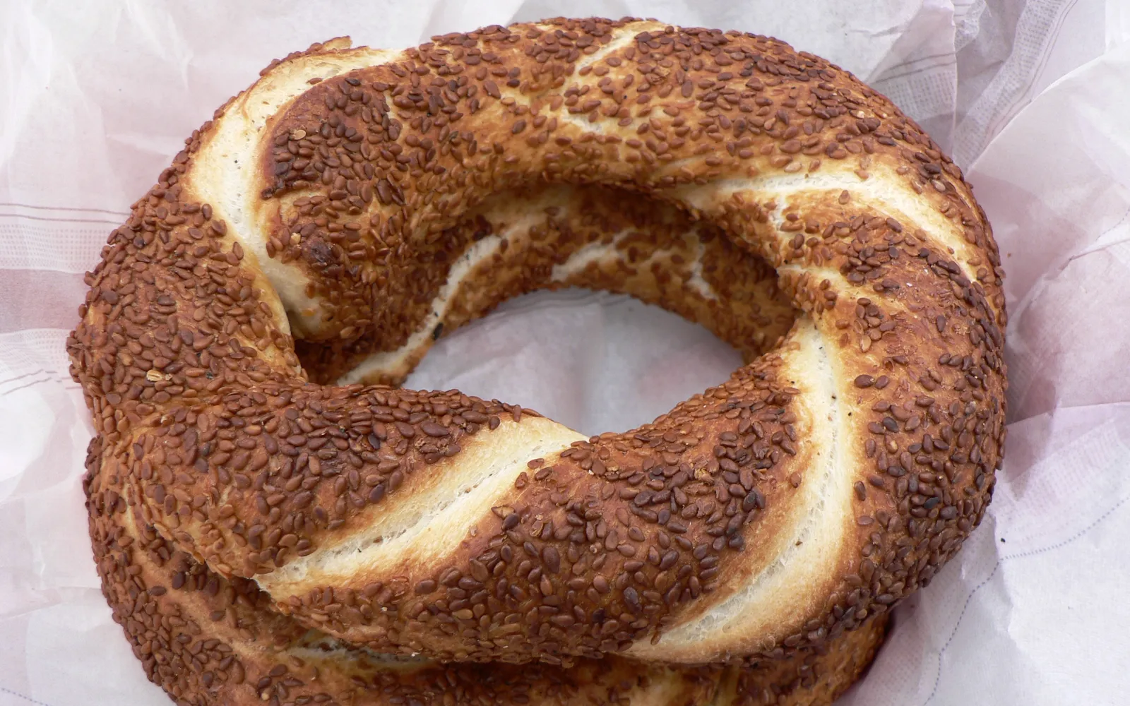 ซิมิตวงกลมเคลือบงาสีทองเรียงบนรถเข็นแดงริมถนนอิสตันบูล พ่อค้าแขวนซิมิตบนราวเหล็กหลายสิบวง