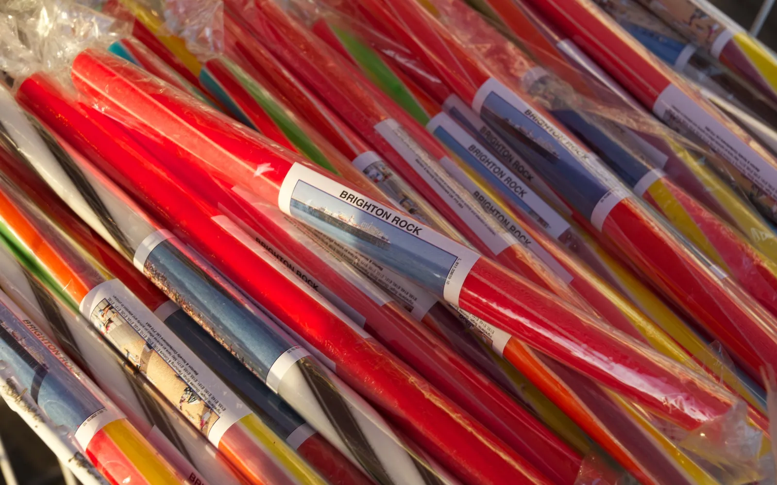 แท่งขนม Brighton Rock สีชมพูพาสเทล ตัวอักษร BRIGHTON วิ่งตลอดความยาวแท่งขนม วางเรียงในถาดกระจก