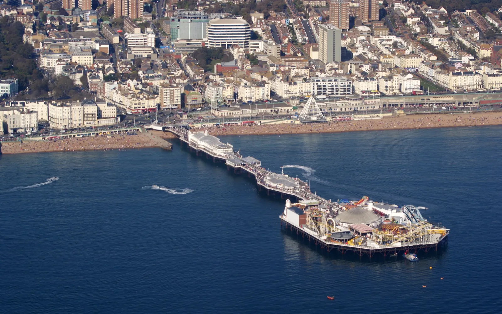 Brighton Palace Pier ยื่นออกสู่ทะเลอังกฤษ โครงสร้างสีขาวกับหอหมุนและเครื่องเล่นสวนสนุกบนสะพานไม้โบราณ