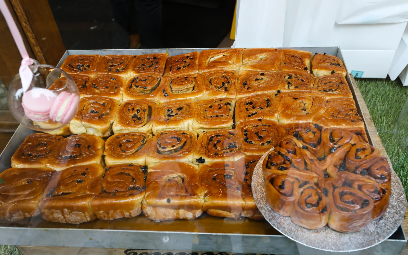 Chelsea Bun ขนมปังขดก้นหอยสีน้ำตาลทองแวววาว เคลือบน้ำตาลหอมหวาน เนื้อด้านในเห็นลูกเกดและเครื่องเทศสีน้ำตาลอ่อน วางบนถาดเบเกอรี่กระดาษขาว