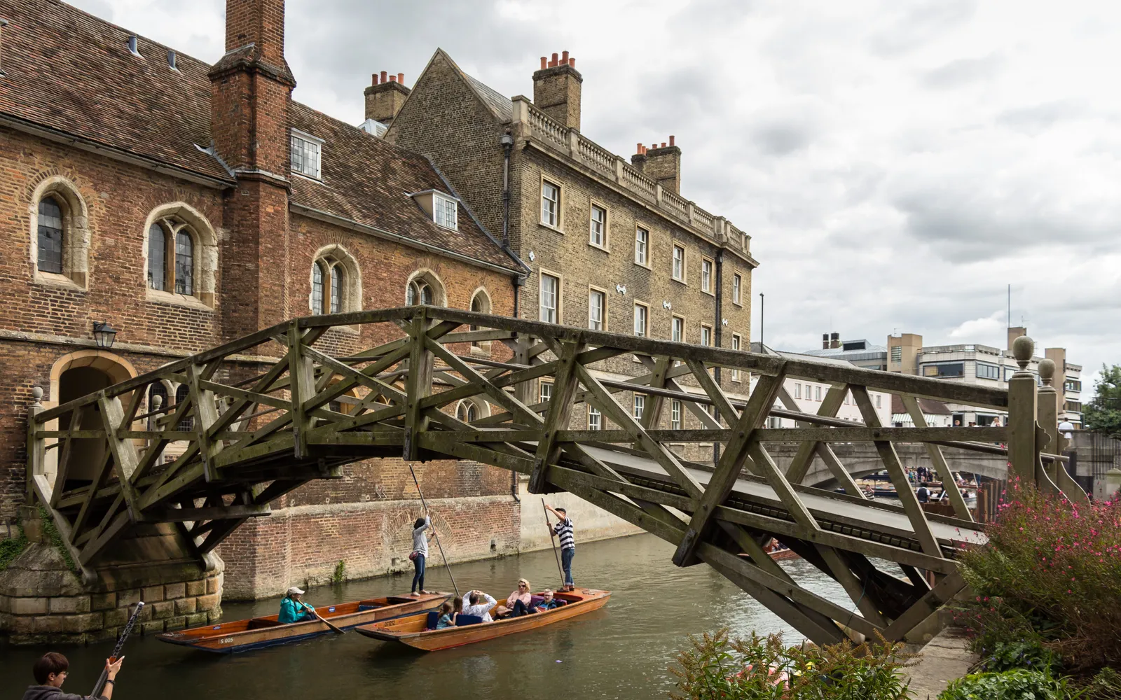 Mathematical Bridge สะพานไม้โค้งสีน้ำตาลอมส้มแห่ง Queens' College เคมบริดจ์ ทอดข้ามแม่น้ำ Cam สีเขียว เรือ Punt ลอยผ่านใต้สะพาน