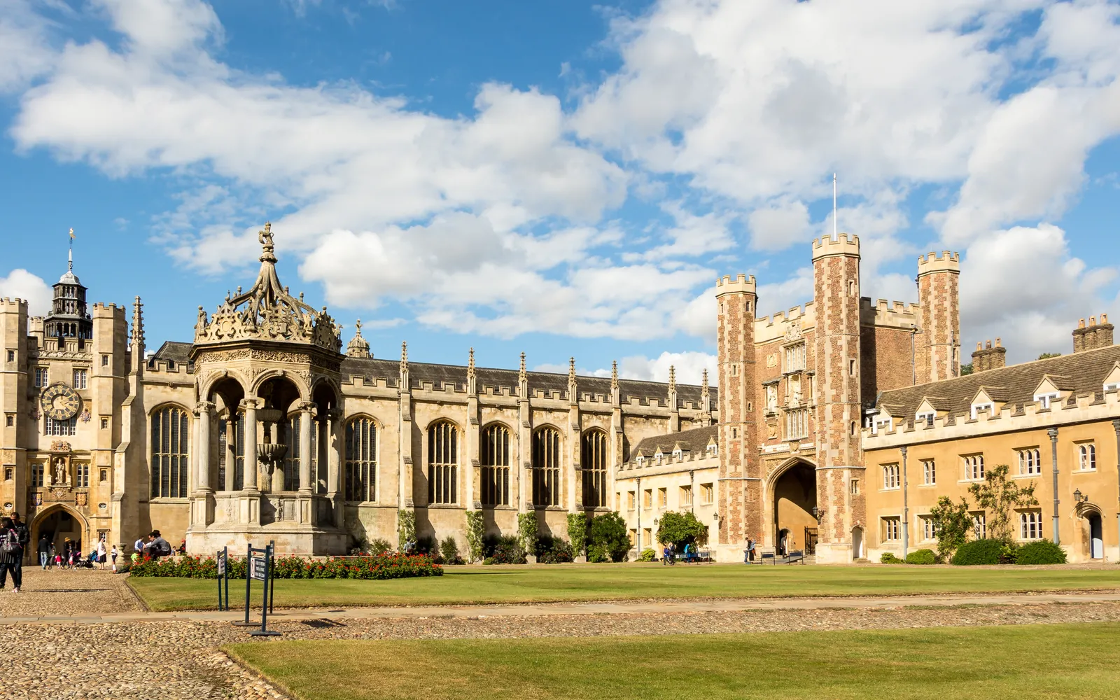 ประตูทางเข้า Great Gate ของ Trinity College เคมบริดจ์ หอคอยหินเทาโบราณประดับด้วยตราอาร์มราชวงศ์และรูปปั้น นักท่องเที่ยวยืนถ่ายรูปด้านหน้า