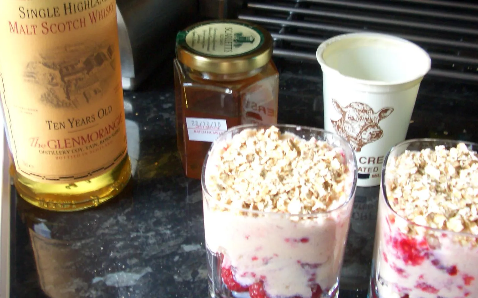 ของหวาน Cranachan ในถ้วยแก้ว วิปครีมนุ่มขาวผสมข้าวโอ๊ตคั่ว ราสเบอร์รีแดงสด และน้ำผึ้งสีทองหยดลงมาด้านบน