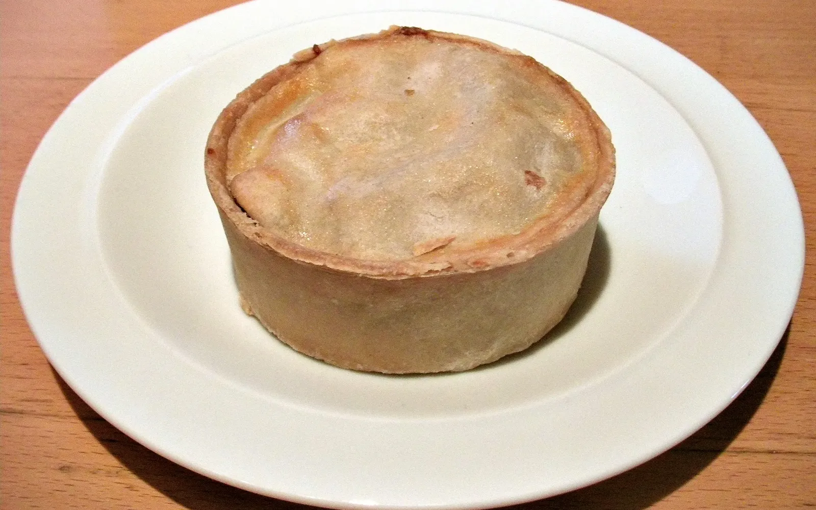 Scotch Pie สกอตแลนด์ทรงกลมเล็กสีน้ำตาลทอง เปลือกแป้งหนาตั้งตรงใส่เนื้อแกะสับปรุงรส วางบนกระดาษห่อตลาด