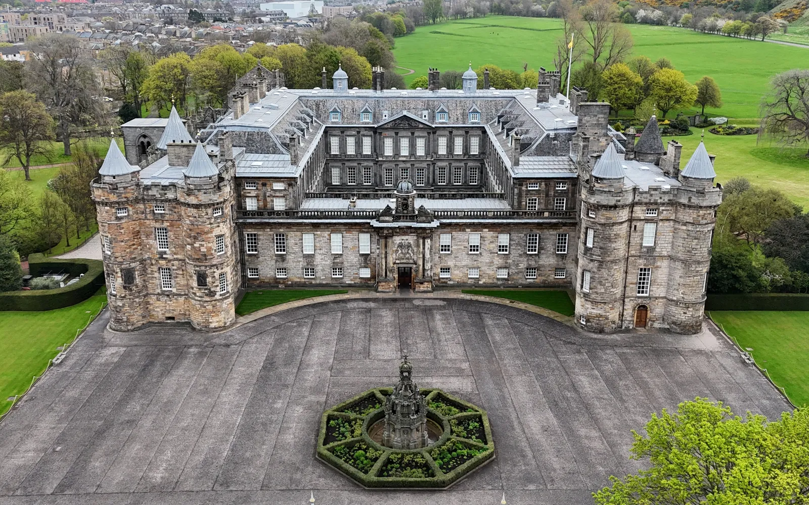 พระราชวัง Holyroodhouse ในเอดินบะระ อาคารหินสีเทาแบบสกอตติชบาร็อคพร้อมหอคอยแฝดทรงกระบอก ล้อมรอบด้วยสนามหญ้าและเนินเขาสีเขียว