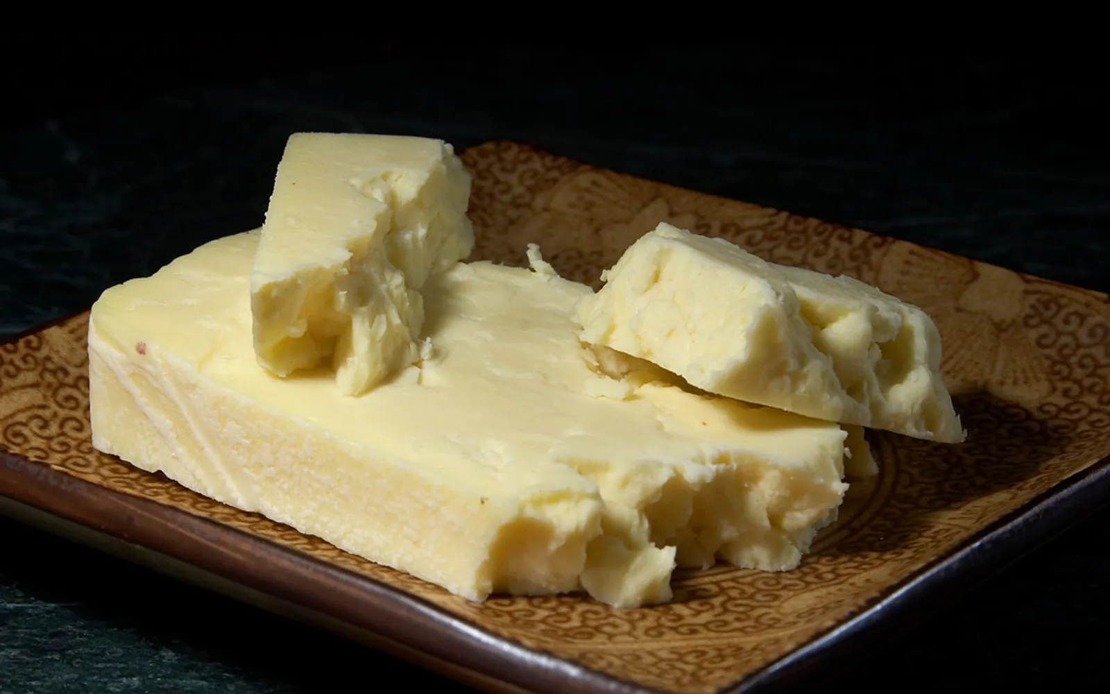 เนยแข็ง Wensleydale สีขาวครีมแผ่นหนาตัดบนเขียงไม้ เนื้อนุ่มร่วนชื้น เสิร์ฟพร้อมแอปเปิลเขียวหั่นบาง ขนมปังโฮลวีทและน้ำผึ้งป่า
