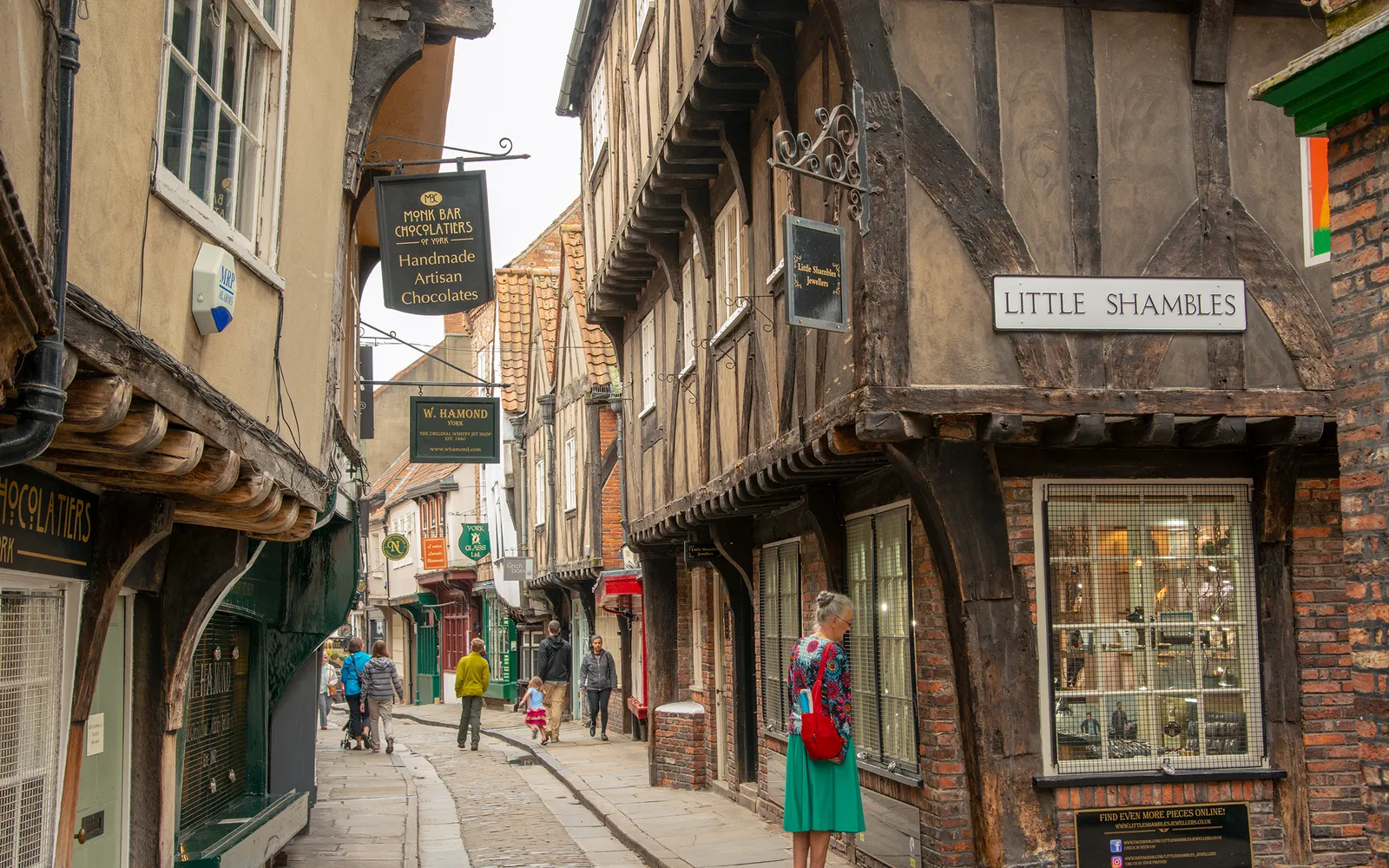 ซอกแคบ The Shambles ในยอร์ก บ้านโครงไม้ยุคกลางสีดำและขาวเอียงโค้งเข้าหากันจนเกือบชนบนหัว แสงอ่อนลอดลงมาตามแนวซอก