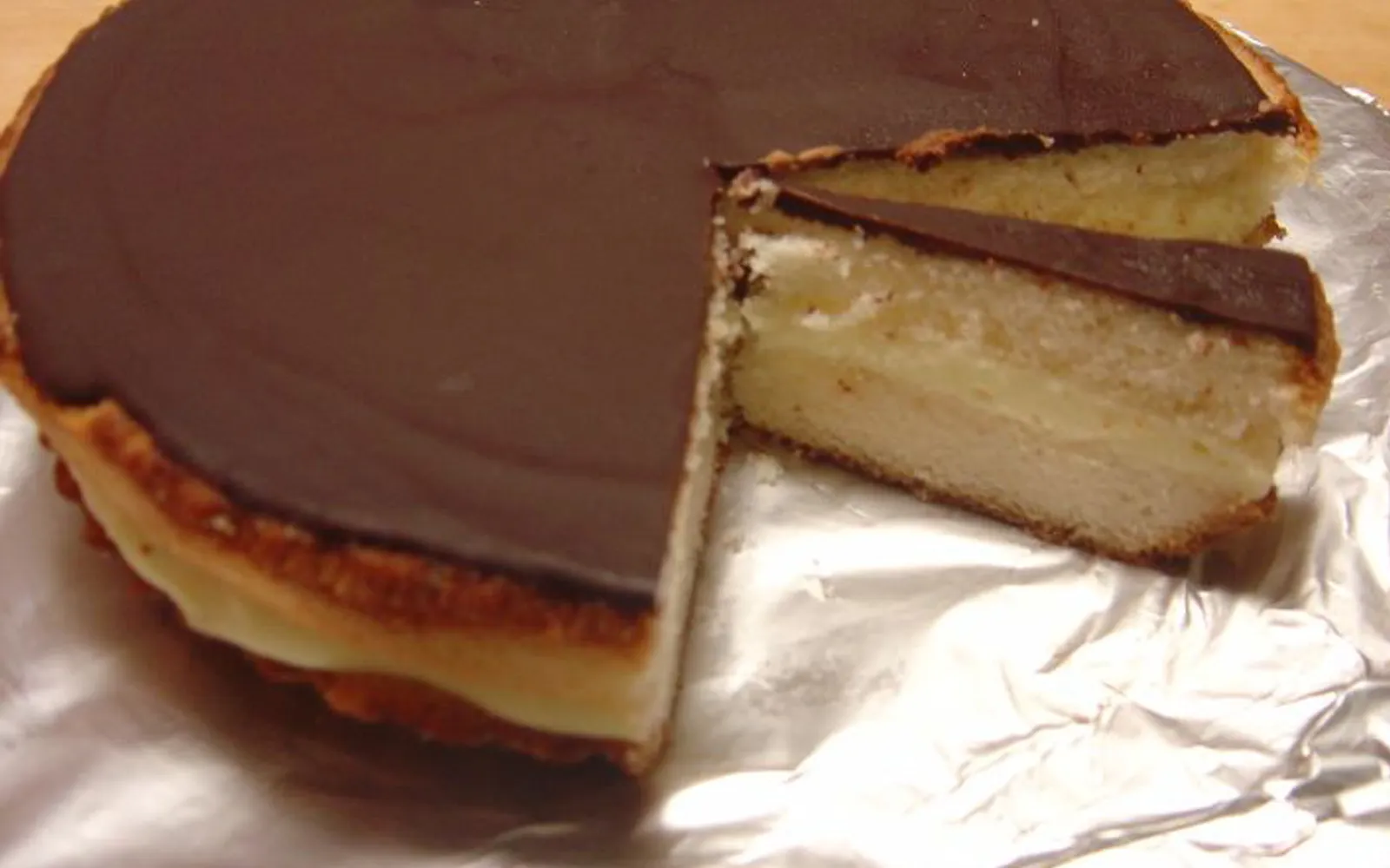 เค้ก Boston Cream Pie หน้าตัดเผยไส้ครีมคัสตาร์ดและสปันจ์เค้ก ราดช็อกโกแลตเงาวาว