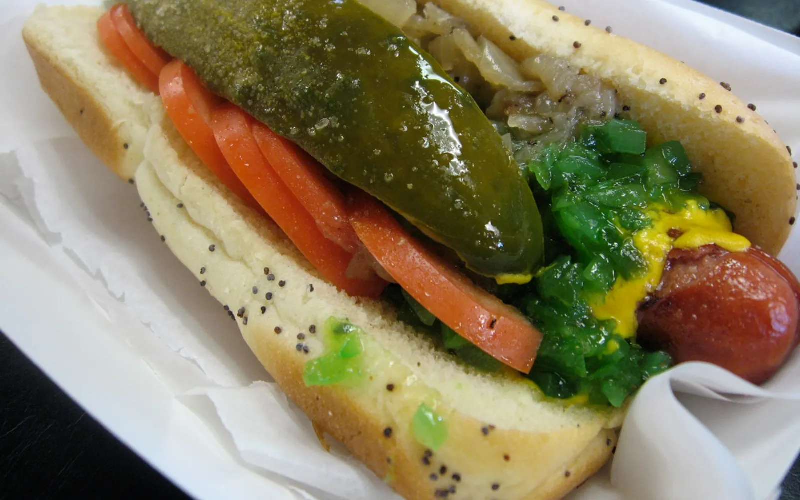 Chicago-style hot dog บนขนมปังนึ่งโรยงาดำ ใส่ท็อปปิ้ง 7 อย่างครบ มัสตาร์ดเหลือง หัวหอม มะเขือเทศ แตงกวาดอง พริกเขียว เกลือเซเลอรี และพิคเคิลรีลิช
