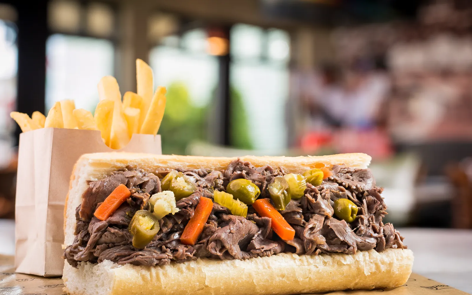 Italian beef sandwich ขนมปังอิตาเลียนแช่น้ำซุปเนื้อชุ่มชื้น หั่นเนื้อวัวบางซ้อนกันหนาพร้อมพริกเขียวย่าง วางบนกระดาษไขน้ำมัน