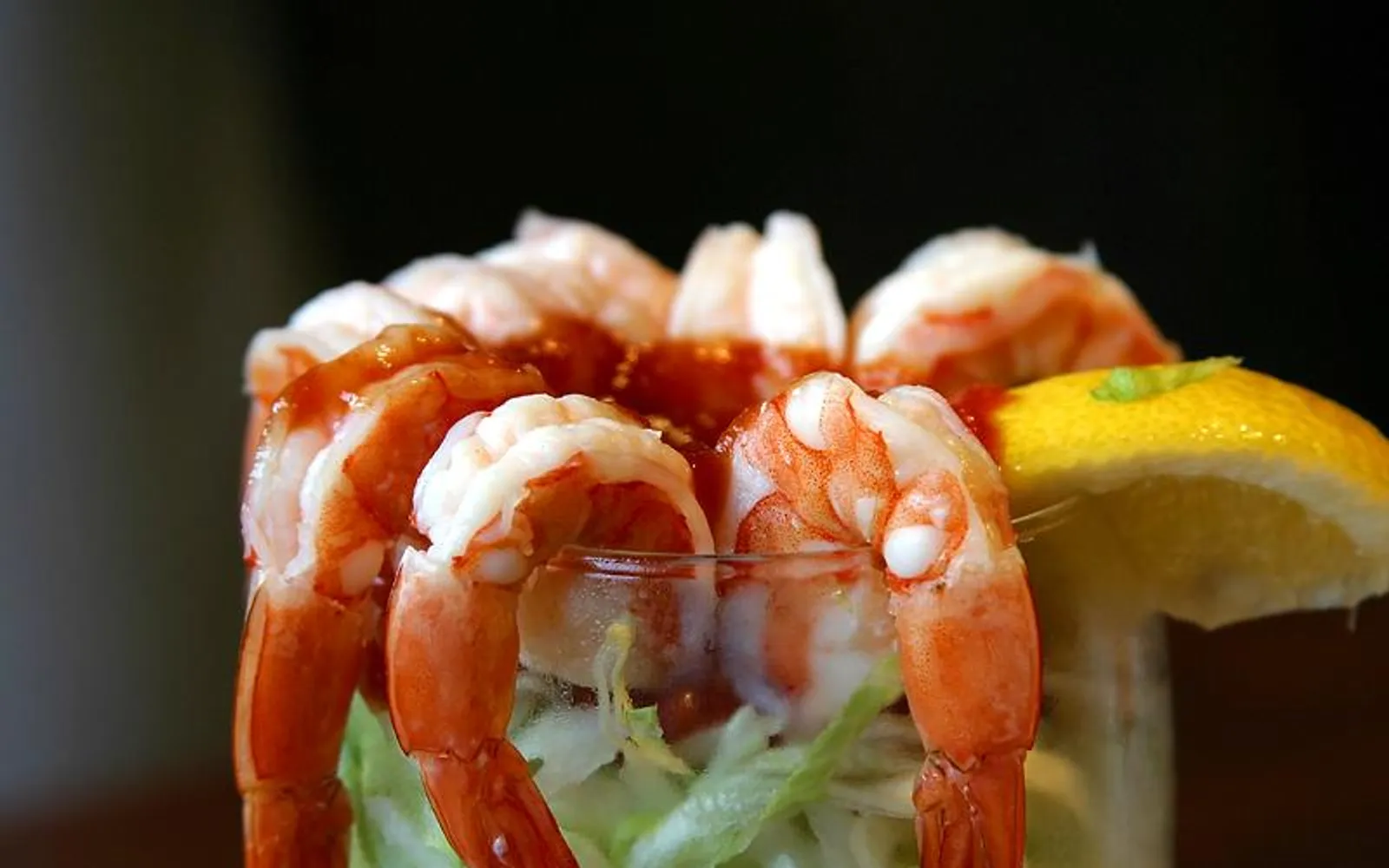 ชริมป์ค็อกเทลแก้วสูงสไตล์คลาสสิก กุ้งตัวใหญ่เรียงขอบแก้วพร้อมซอส cocktail สีแดงตรงกลาง บนเคาน์เตอร์ไม้ดำเก่าแก่ของ Golden Gate Casino