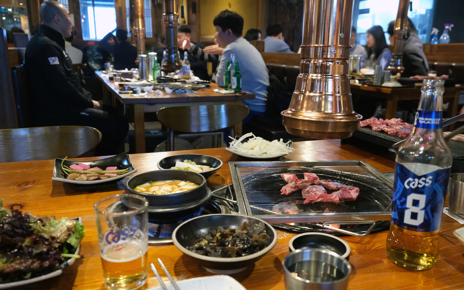 เตาถ่านในร้าน Korean BBQ LA เนื้อ Galbi หมักซอสเกาหลีย่างอยู่บนตะแกรง ล้อมรอบด้วยเครื่องเคียง banchan หลากสี