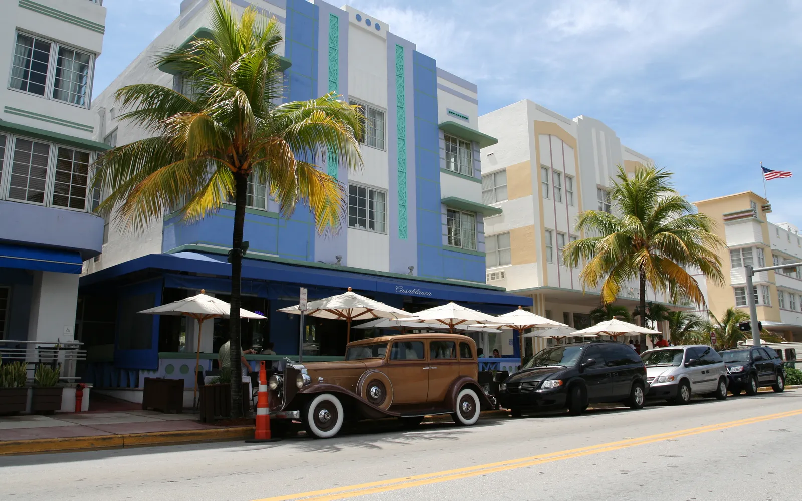 ถนน Ocean Drive ไมแอมีบีชยามพลบค่ำ อาคารสไตล์อาร์ตเดโกทาสีพาสเทลชมพูเหลืองและเขียวมิ้นต์เรียงรายสองข้างทาง ไฟนีออนสีส้มสะท้อนผิวถนนเปียก