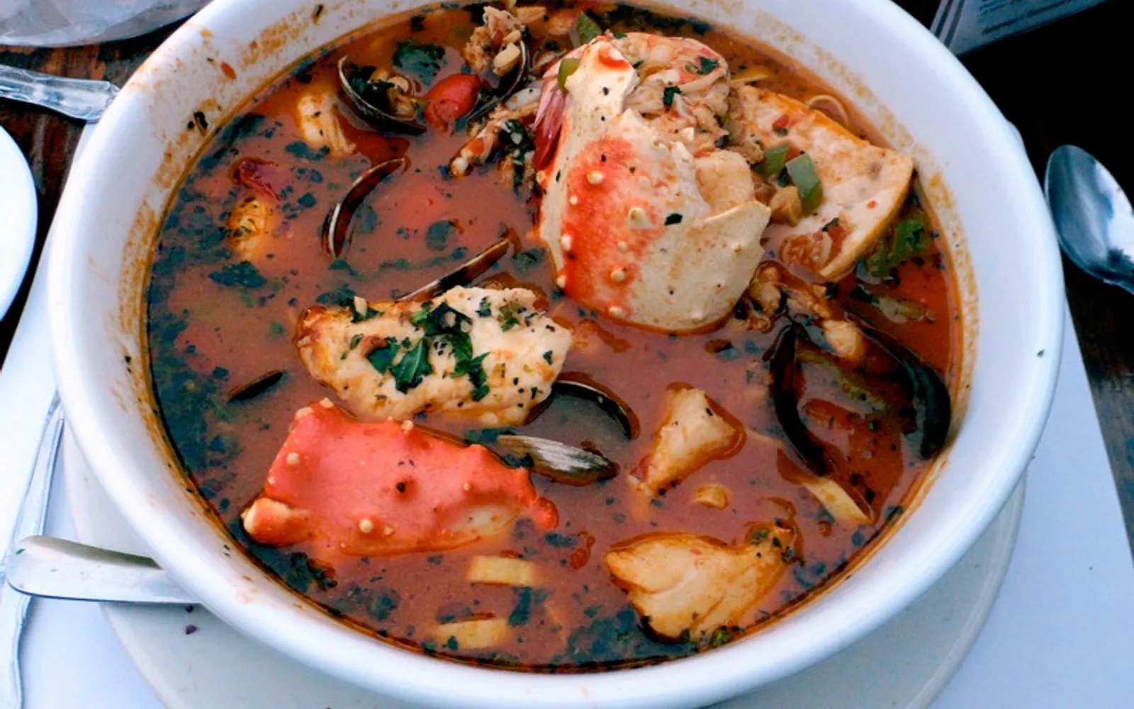 ซุป cioppino สีแดงเข้มเต็มไปด้วยปู หอย กุ้ง และปลาในชามใหญ่