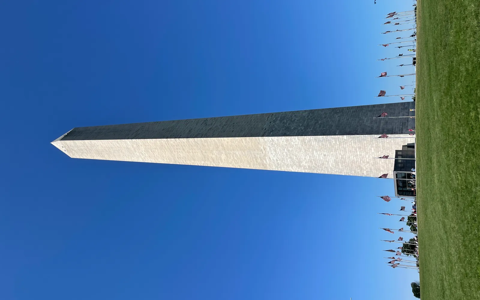 อนุสาวรีย์วอชิงตันสูง 169 เมตรตั้งตระหง่านกลาง National Mall ล้อมรอบด้วยธงชาติอเมริกัน 50 ผืน ท้องฟ้าสีฟ้าครามเป็นฉากหลัง