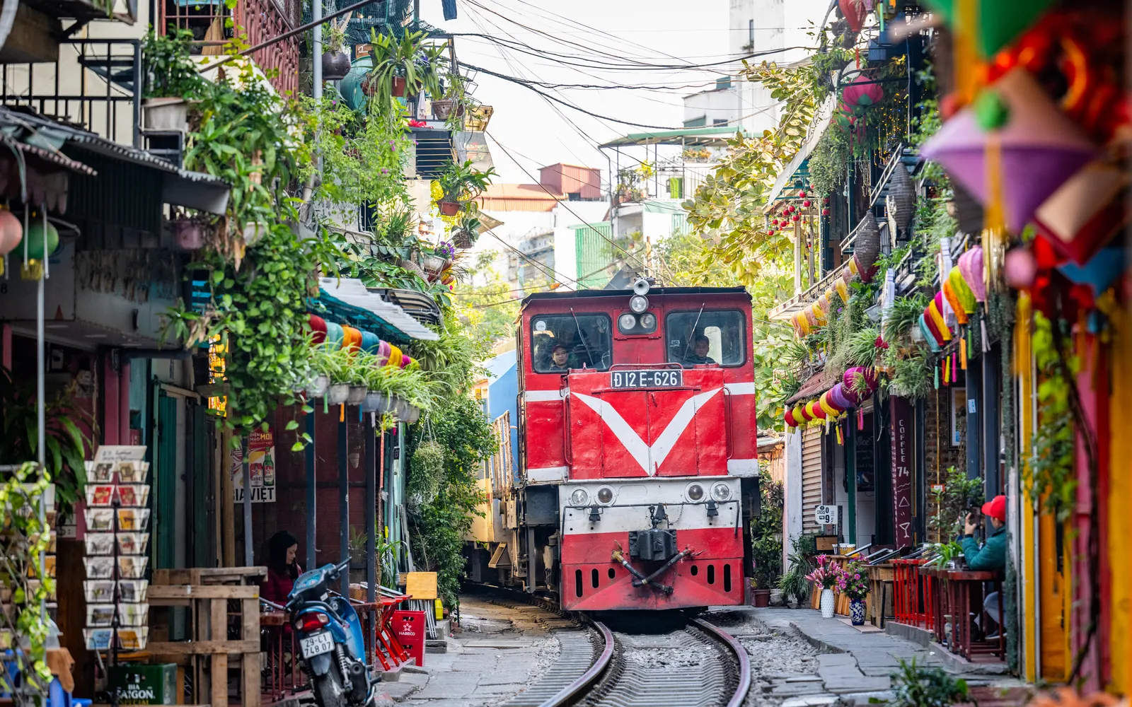 รถไฟวิ่งผ่านถนนแคบที่มีบ้านเรือนอยู่ชิดกันสองข้างทางในย่านถนนรถไฟฮานอย